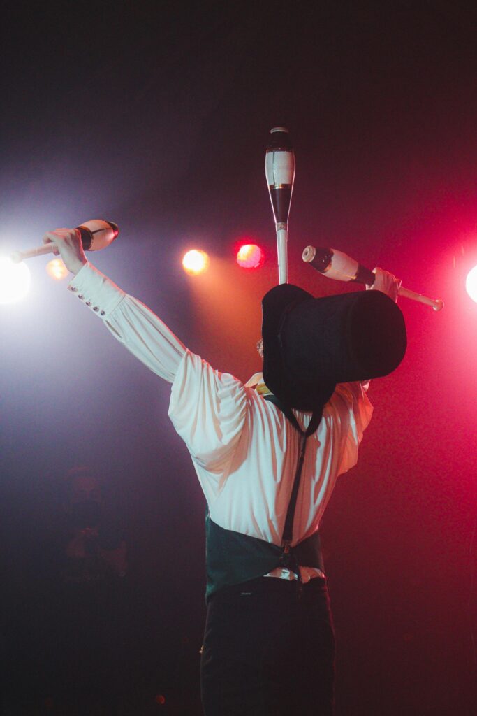 A circus performer juggles clubs under vibrant stage lighting, showcasing skill and entertainment.