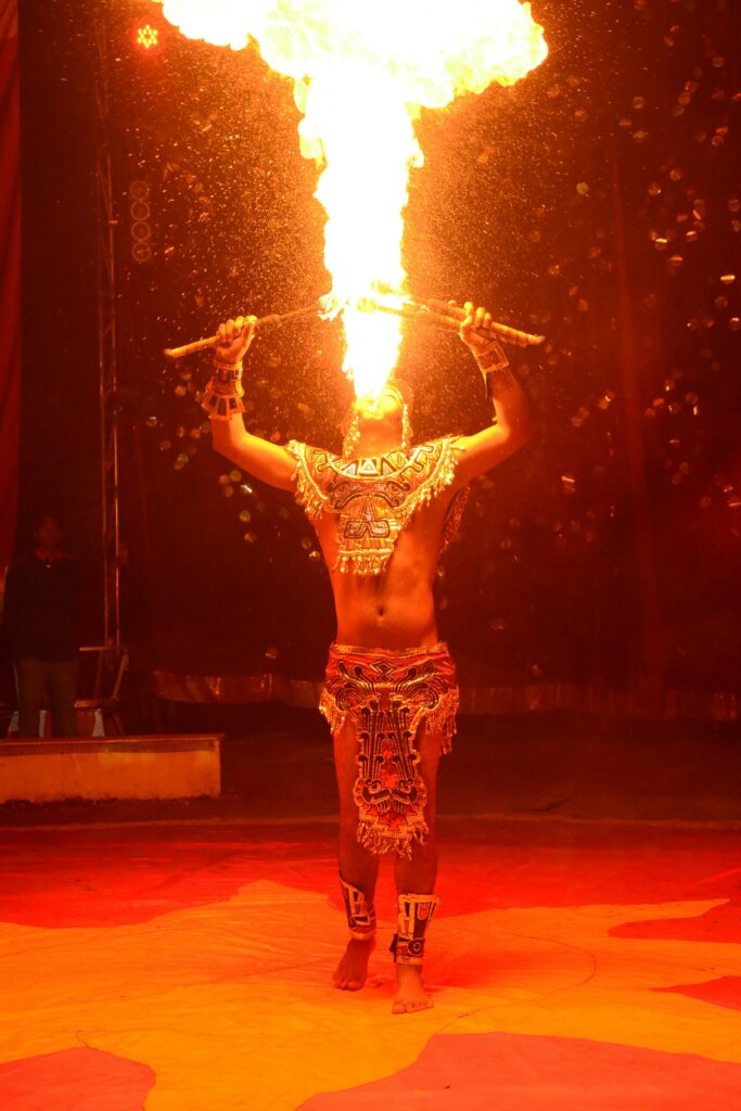 Dynamic fire breather performing in traditional costume during an energetic night show.